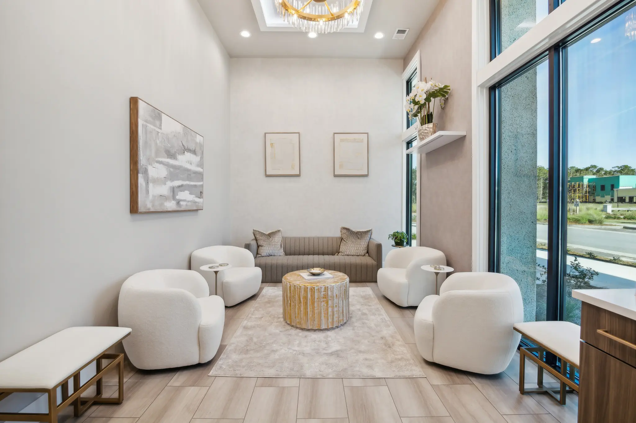 The lounge at The Bluffs — cream bouclé chairs, taupe sofa, and a chandelier by floor-to-ceiling windows